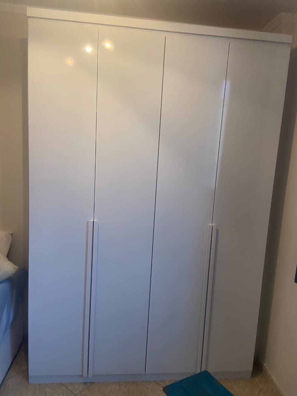Guarda-roupa branco de quatro portas com puxadores embutidos, montado ao lado da cama